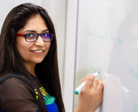 female student writing on a whiteboard and smiling
